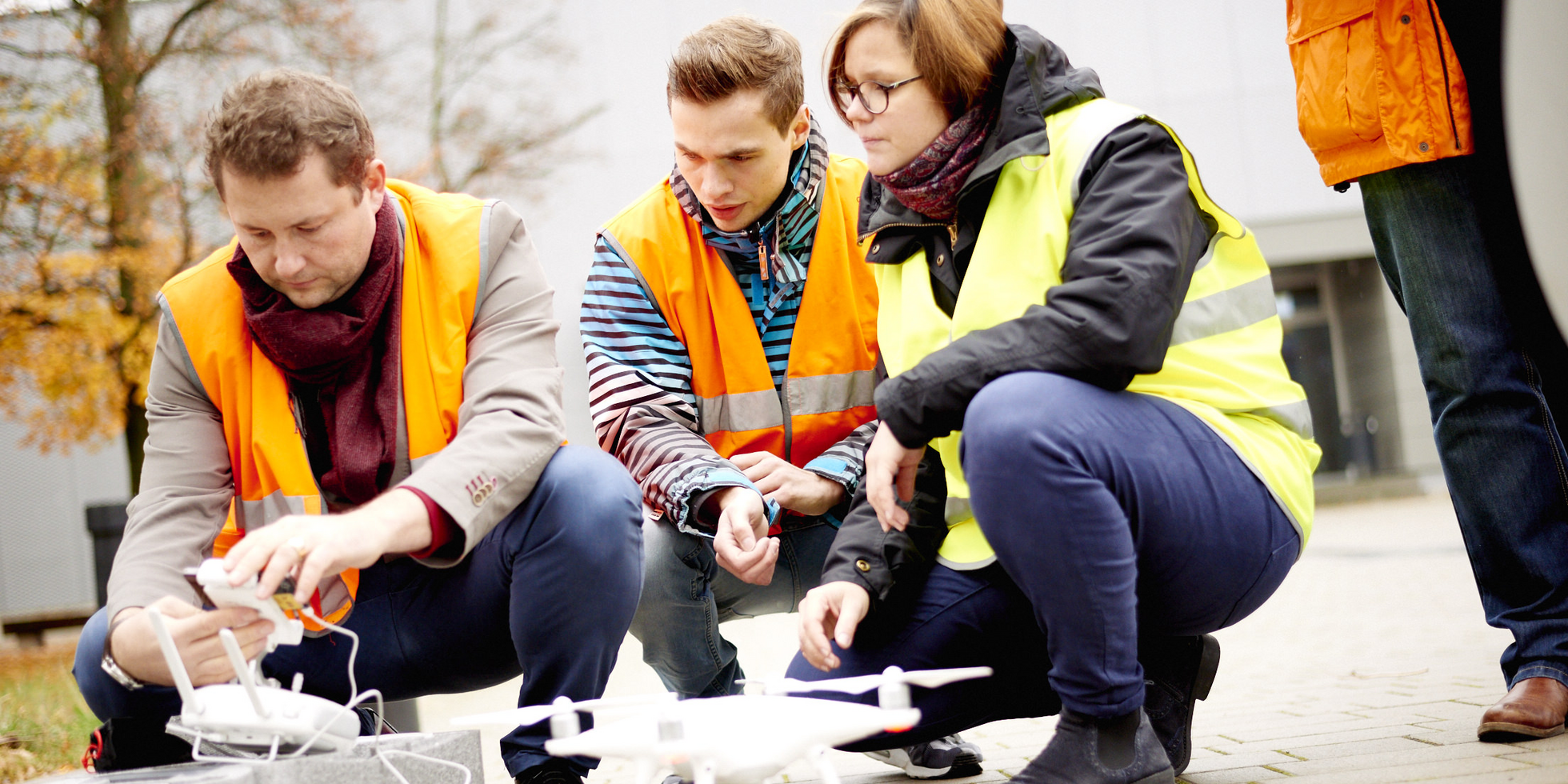 Three people crouching in front of a drone