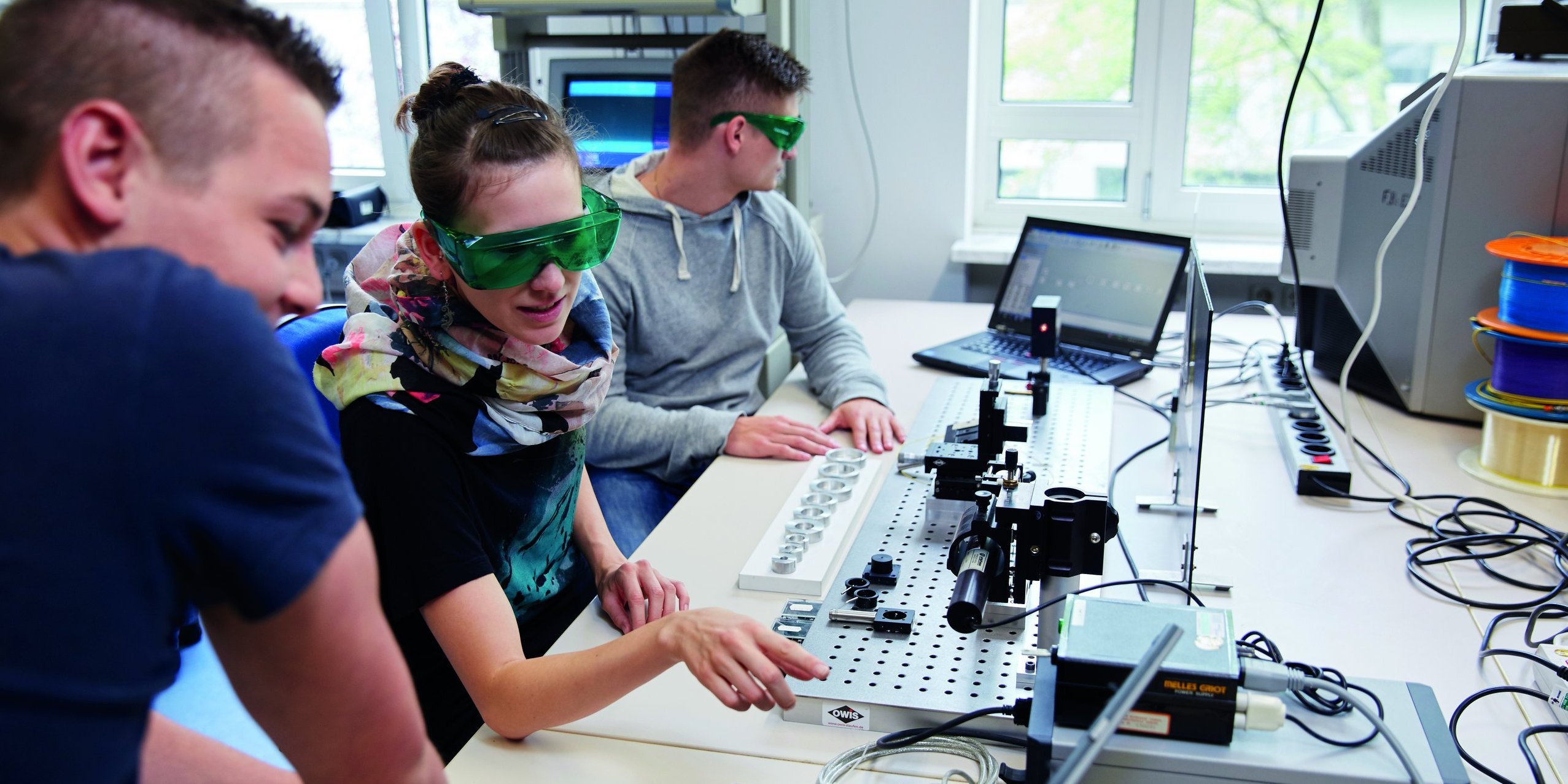 People, some with protective goggles, in front of technical equipment