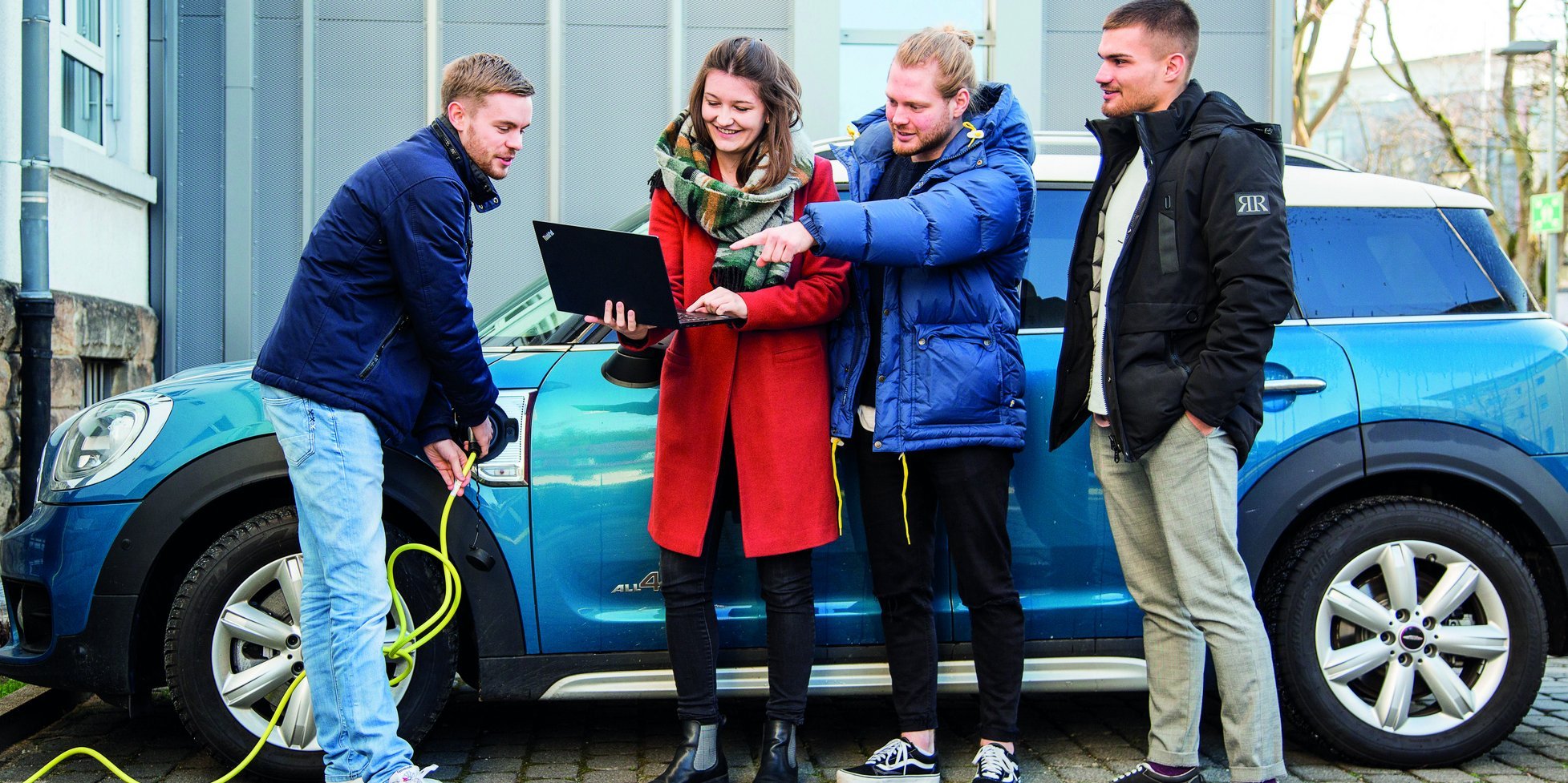 Vier Personen mit Notebook vor einem Elektroauto