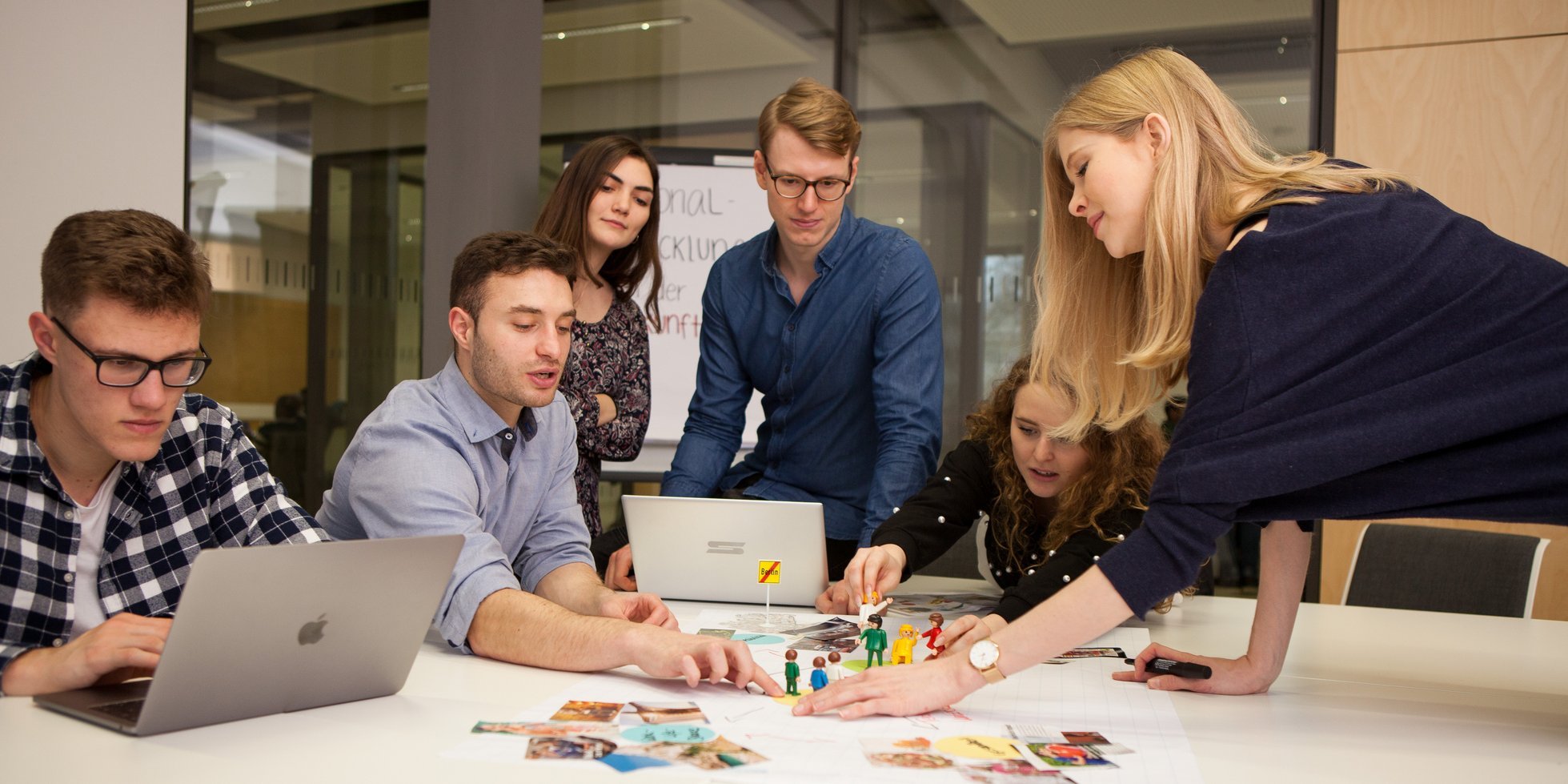 fünf Personen rund um ein Flipchart mit Bildern und Spielfiguren