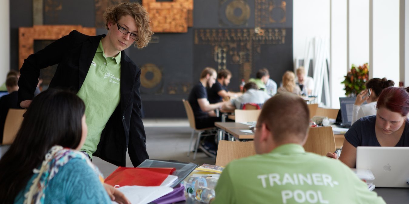 Zwei Studierenden sitzen am Tisch und lernen. Eine weitere Studentin steht vor dem Tisch und unterhält sich mit den zwei Studierenden. Das Bild wurde auf der "Langen Nacht der Hausarbeiten" an der Hochschule Darmstadt im Jahr 2012 aufgenommen.