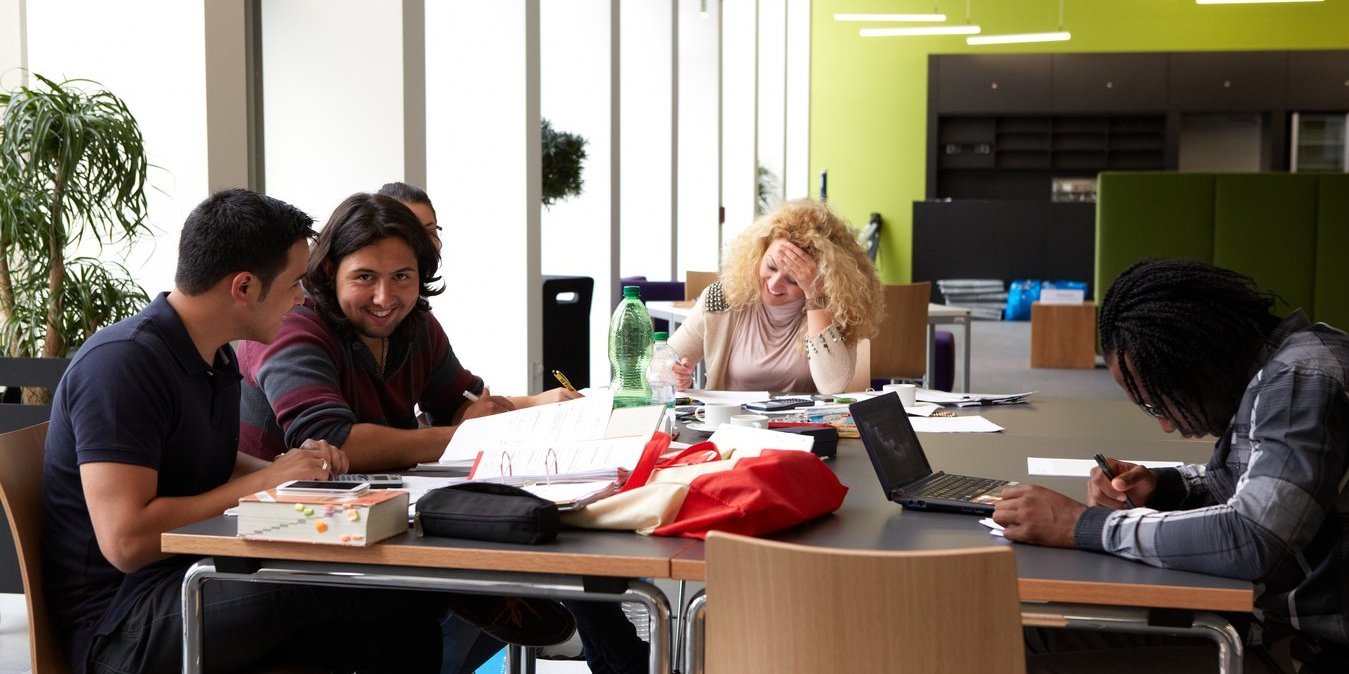 Bier Studierende sitzen an einem Tisch und lernen. Auf dem Tisch liegen Bücher und Skripte.